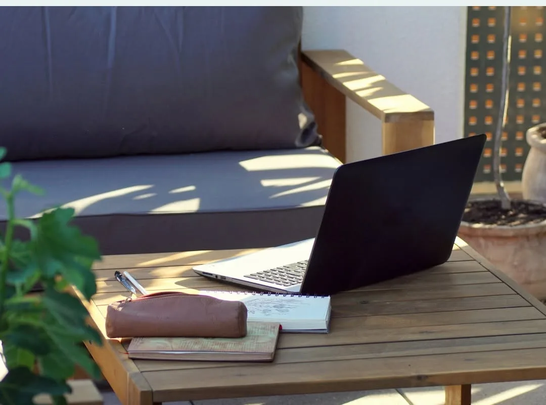 Laptop and notebook on an outdoor table beneath a shaded veranda